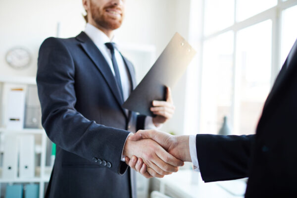 Young successful broker with document shaking hand of business partner after signing contract in office